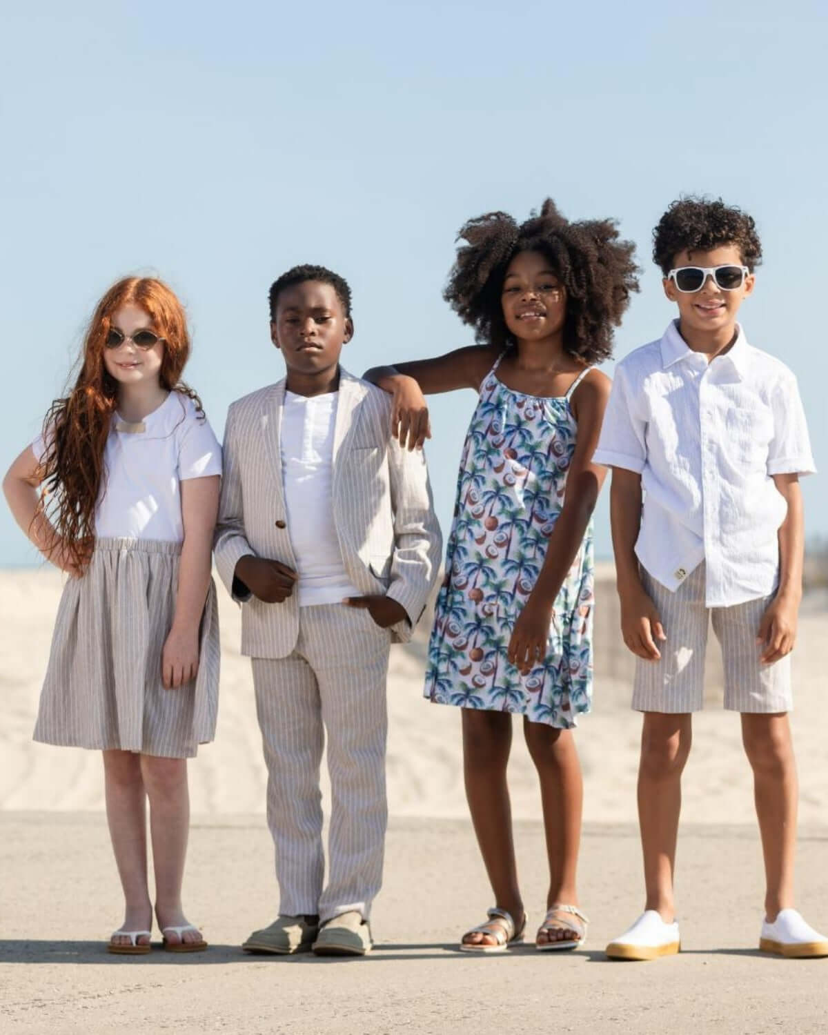 Four stylish kids in trendy summer outfits on a beach, showcasing playful fashion versatility.