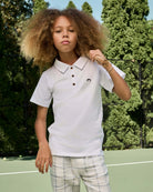 Child wearing a white polo shirt with a small black logo on a tennis court