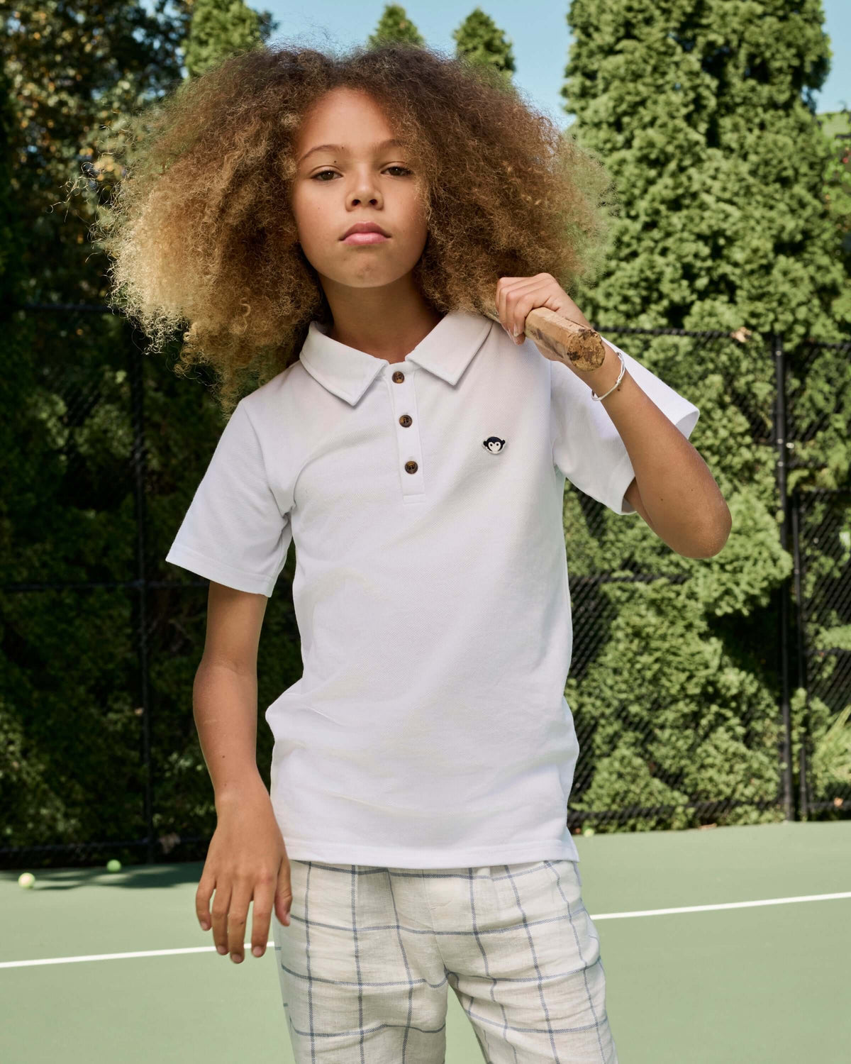 Child wearing a white polo shirt with a small black logo on a tennis court
