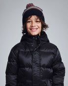 Child wearing a Navy Blue Wind Hat with a pom pom, smiling in a black puffer jacket.