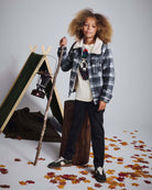 Child wearing a Winter Dog Graphic Long Sleeve Tee under a cozy plaid jacket, surrounded by autumn leaves.