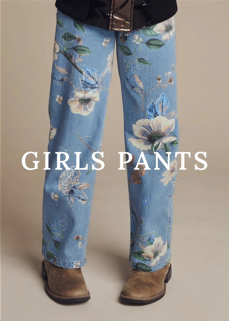 A person wearing light blue floral jeans with white flowers, green leaves, and butterflies, paired with brown boots against a beige studio background. Large white text across the lower half reads 'GIRLS PANTS'.