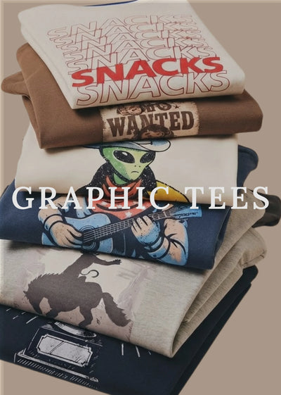 A stack of folded graphic T-shirts displayed on a plain beige background. The top shirt is off-white with repeated 'SNACKS' text in red and brown, the next is brown with a distressed 'WANTED' patch graphic, then a cream shirt with a green alien playing guitar, followed by a dark blue shirt with a cowboy silhouette, and a dark navy shirt with a cassette graphic.
