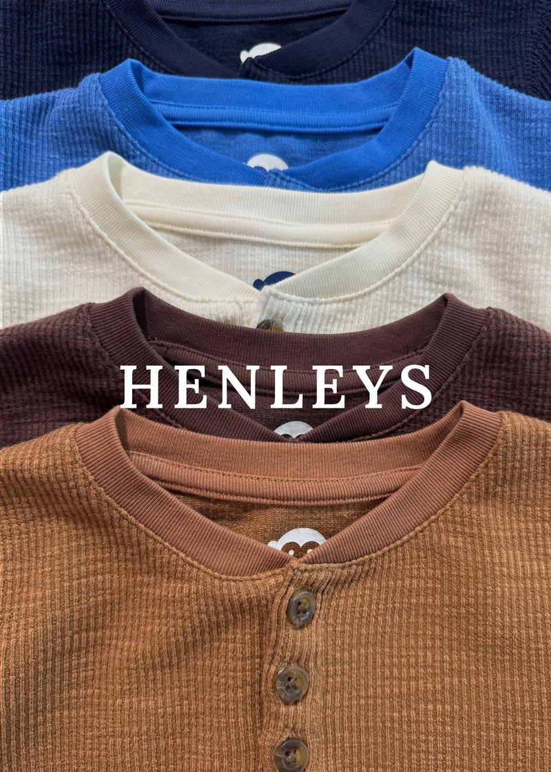 Four ribbed henley shirts stacked vertically in navy, blue, cream, and brown, with a large white 'HENLEYS' logo text overlay across the center.