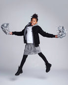 Girl jumping joyfully in a Silver Hearts Bomber Jacket with silver pom-poms for a fun and fashionable look.