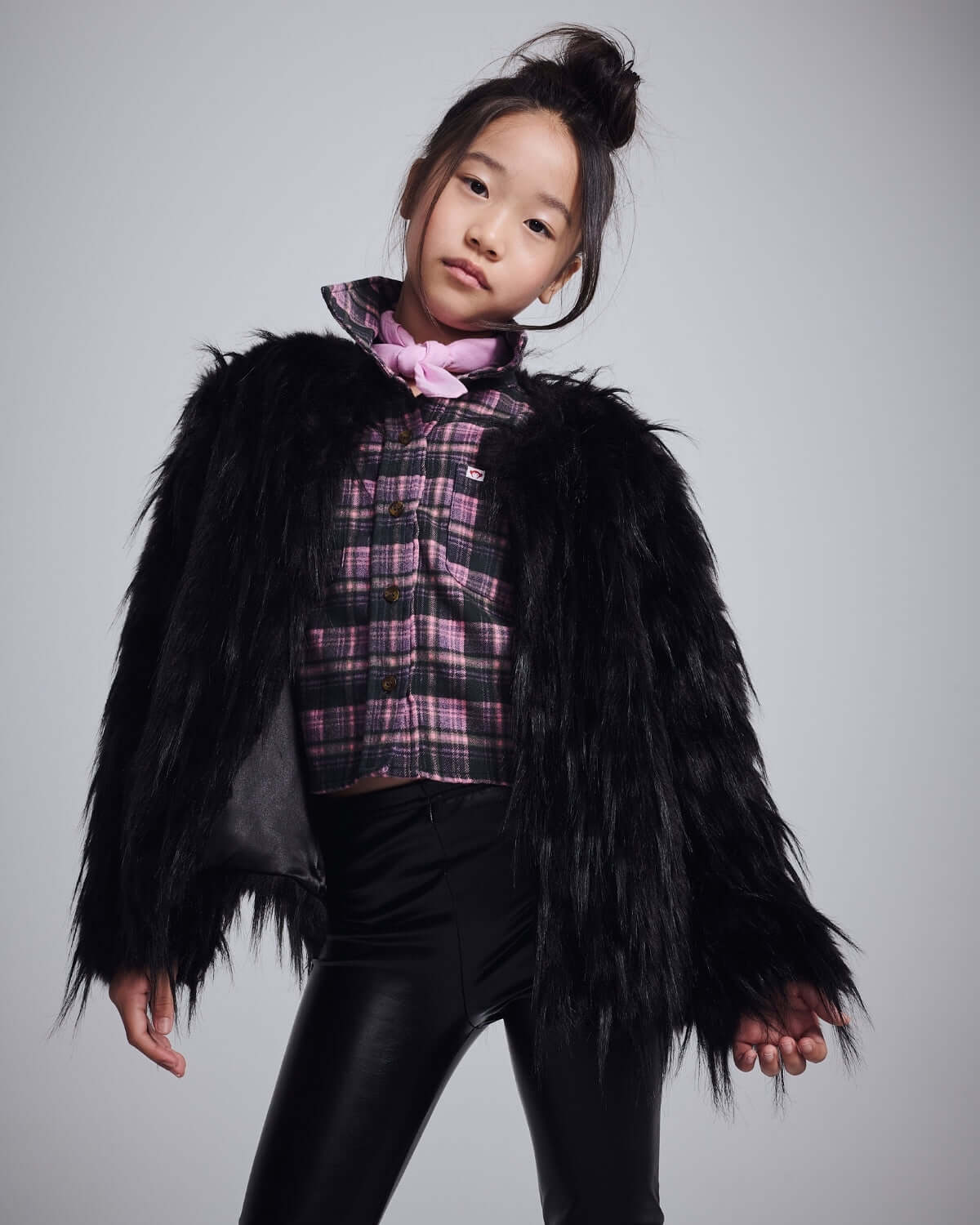 Stylish girl wearing a Black Faux Fur Coat over a plaid shirt, showcasing warmth and fashion for chilly days.