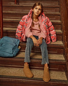 Girl sitting on stairs wearing a pink floral puffer jacket, pink sweater, denim pants, and brown boots.