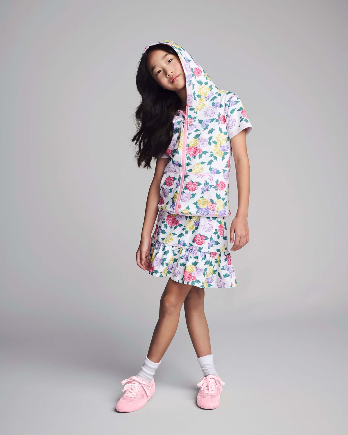 Young girl wearing a floral outfit with pink shoes on a gray background