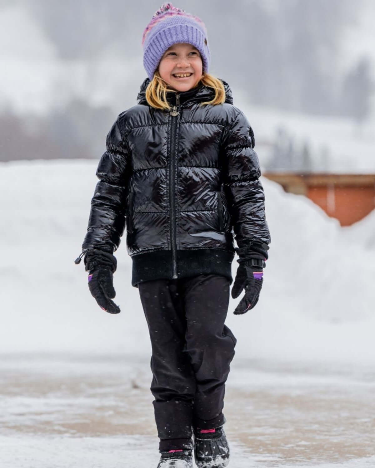 Child wearing a Shiny Black Flurry Coat walking in the snow, showcasing style and warmth.