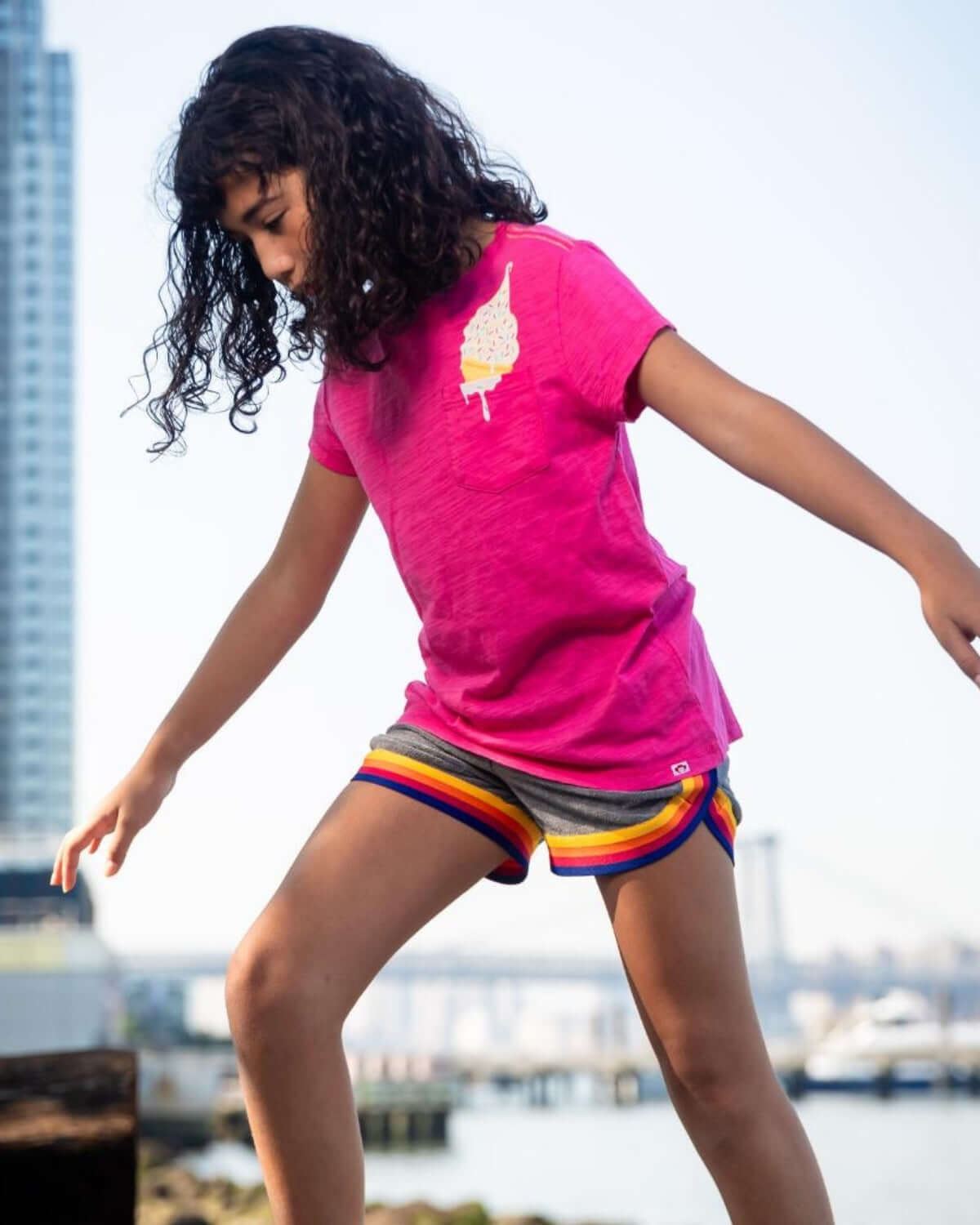 Girl wearing Grey Lori Shorts and a pink shirt, playing outdoors near a waterfront.