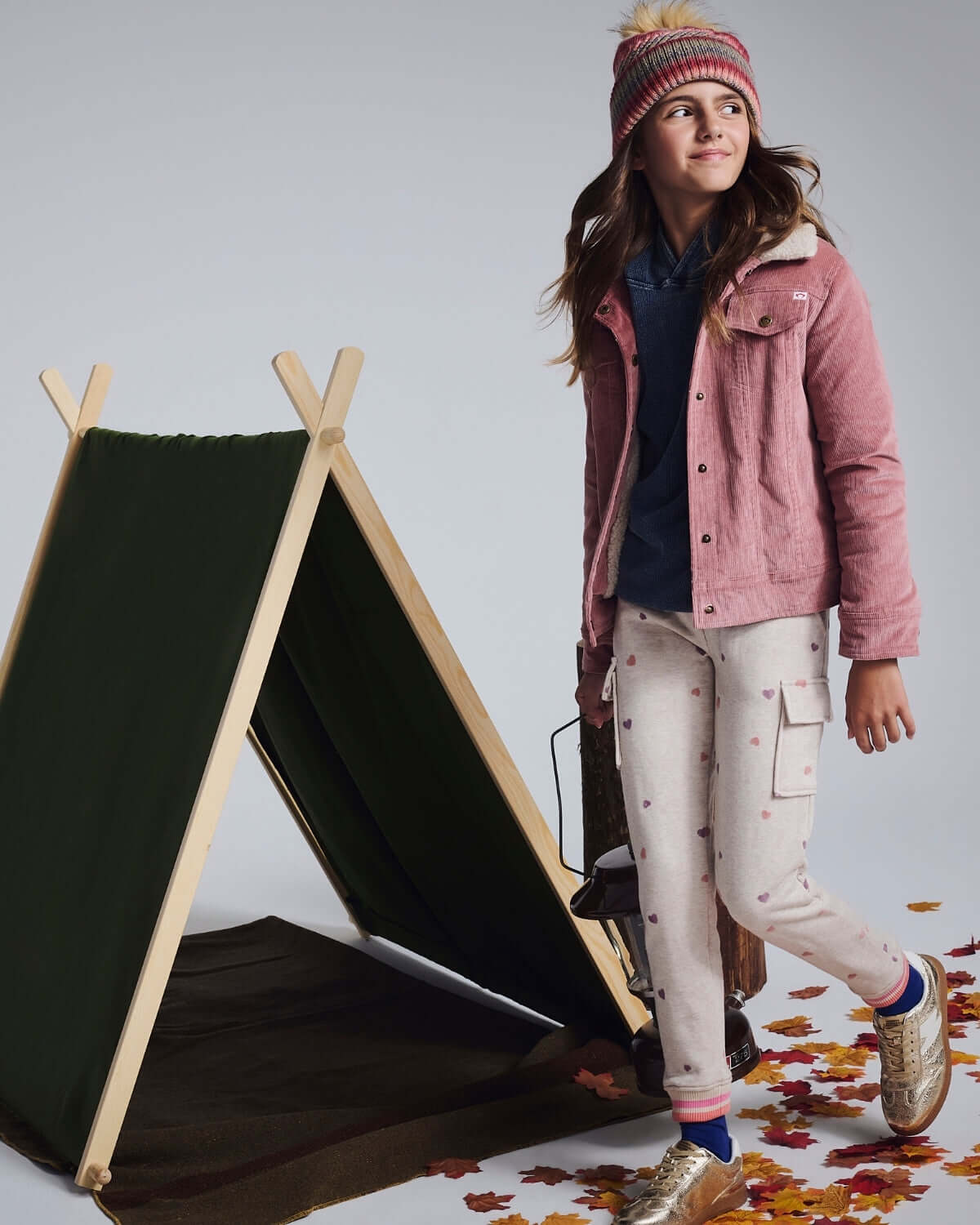 Girl wearing Heart Oatmeal Cozy Cargo Joggers and a pink jacket by a tent outdoors.