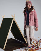 Girl wearing Heart Oatmeal Cozy Cargo Joggers and a pink jacket by a tent outdoors.
