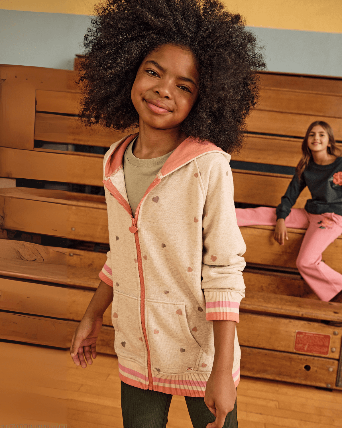 Heart Oatmeal Cozy Raglan Hoodie worn by a smiling girl, featuring pink and orange hearts, perfect for cozy adventures.