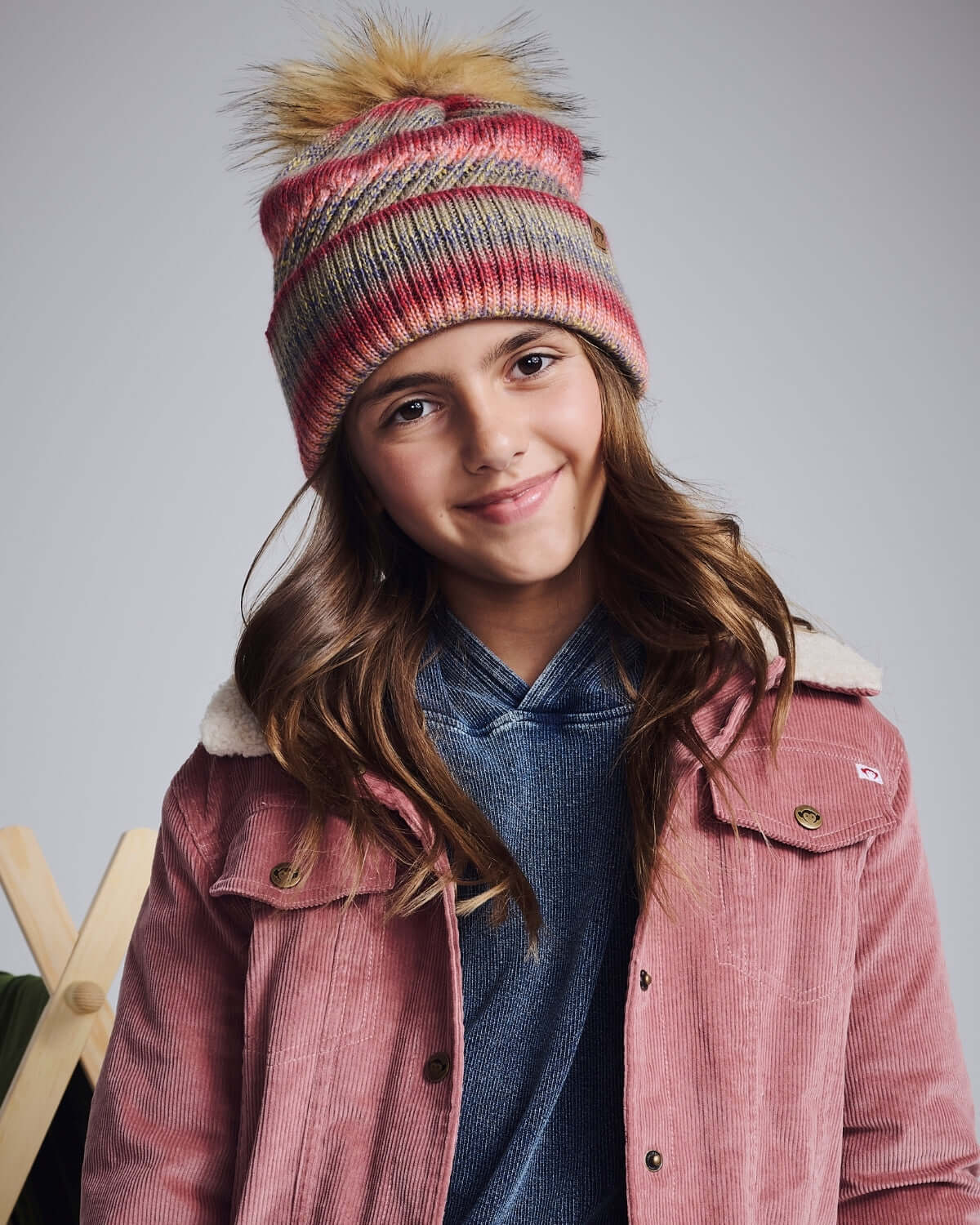 Young girl wearing a Rose Iris Pom Beanie with a playful pom pom and cozy winter outfit.