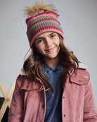 Young girl wearing a Rose Iris Pom Beanie with a playful pom pom and cozy winter outfit.