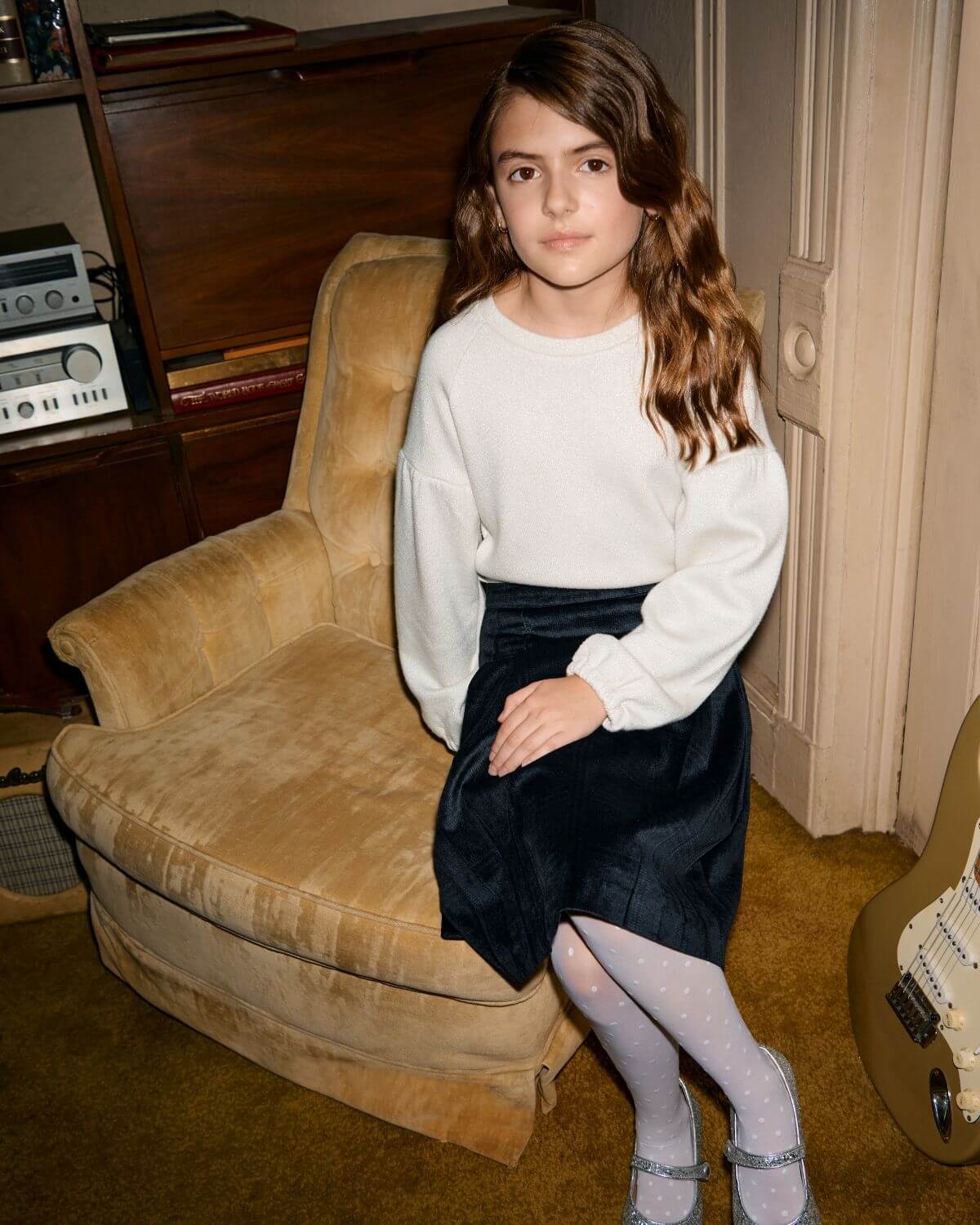 White Shine Julie Tee worn by a young girl, sitting on a chair, styled with a black skirt and classic accessories.