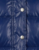 Close-up of a shiny royal blue quilted puffer jacket with silver snap buttons featuring a heart logo.