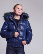 A child wearing a shiny navy blue puffer jacket with a dark faux-fur hood, photographed against a plain light gray studio background.