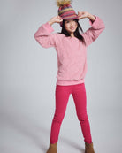Girl wearing Rose Leggings in vibrant pink, paired with a fluffy pink sweater and a colorful hat.