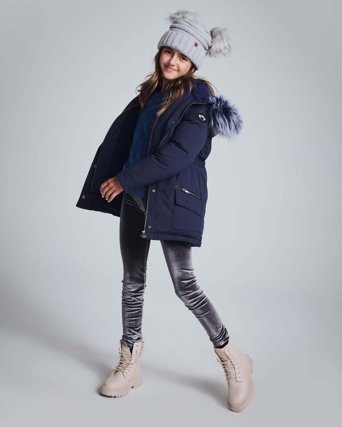 A girl wearing a navy coat and silver frost leggings, showcasing style and comfort in a playful pose.