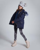 A girl wearing a navy coat and silver frost leggings, showcasing style and comfort in a playful pose.