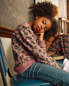 Leopard Ruby Sweatshirt worn by a young girl, showcasing a lilac leopard print design in a classroom setting.