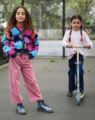 Two kids playing outside, one wearing Dusty Rose Liana Jeans and a colorful cardigan, the other on a scooter.