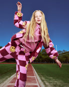 Girl wearing a Pink Melanie Sherpa Jacket with smiley face details, posing playfully on a sports track.