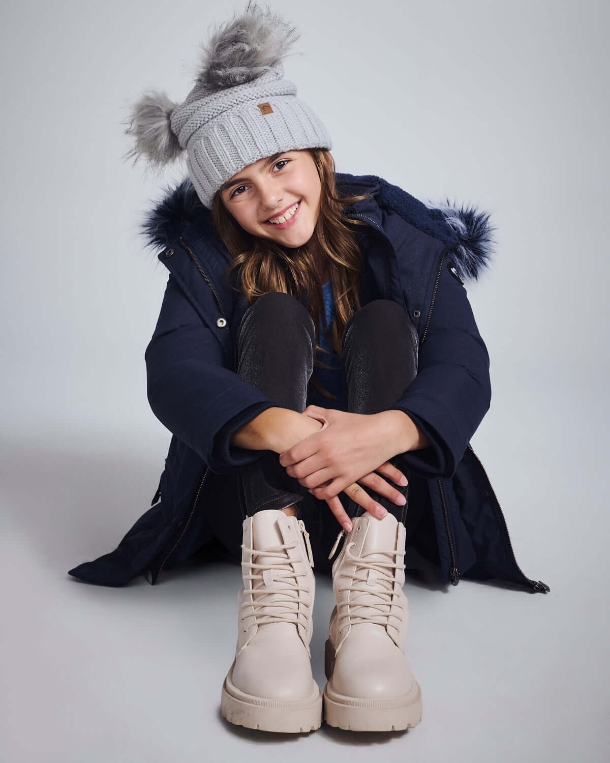 Girl wearing a Navy Sparkle Middie Puffer Coat with a cozy hat and stylish boots.
