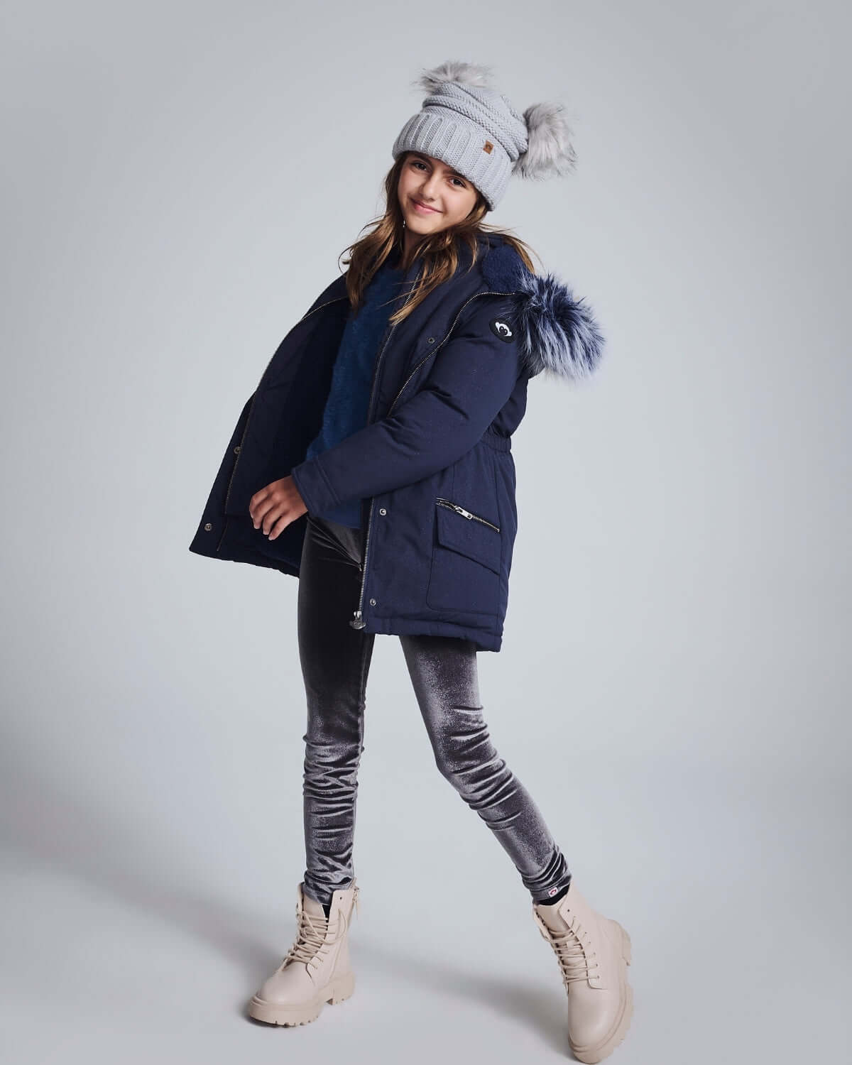 Girl wearing a Navy Sparkle Middie Puffer Coat with a faux fur hood, styled with shiny leggings and winter boots.