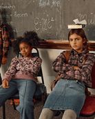 Two kids sitting in a classroom wearing comfortable styles, featuring a Midi Denim Skirt and playful sweaters.