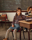 Girl in plaid shirt and Midi Denim Skirt sitting at a school desk with classmates in a classroom.