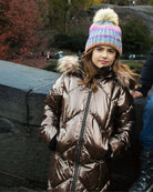 Copper Nova Long Coat worn by a girl with a colorful hat, featuring faux fur hood in a natural setting.