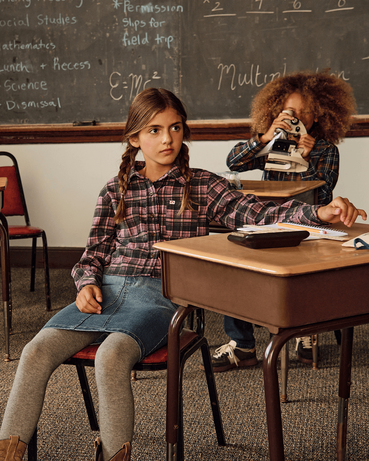 Girl wearing Pink Plaid Polly Cropped Flannel in classroom setting, looking focused with a classmate in the background.