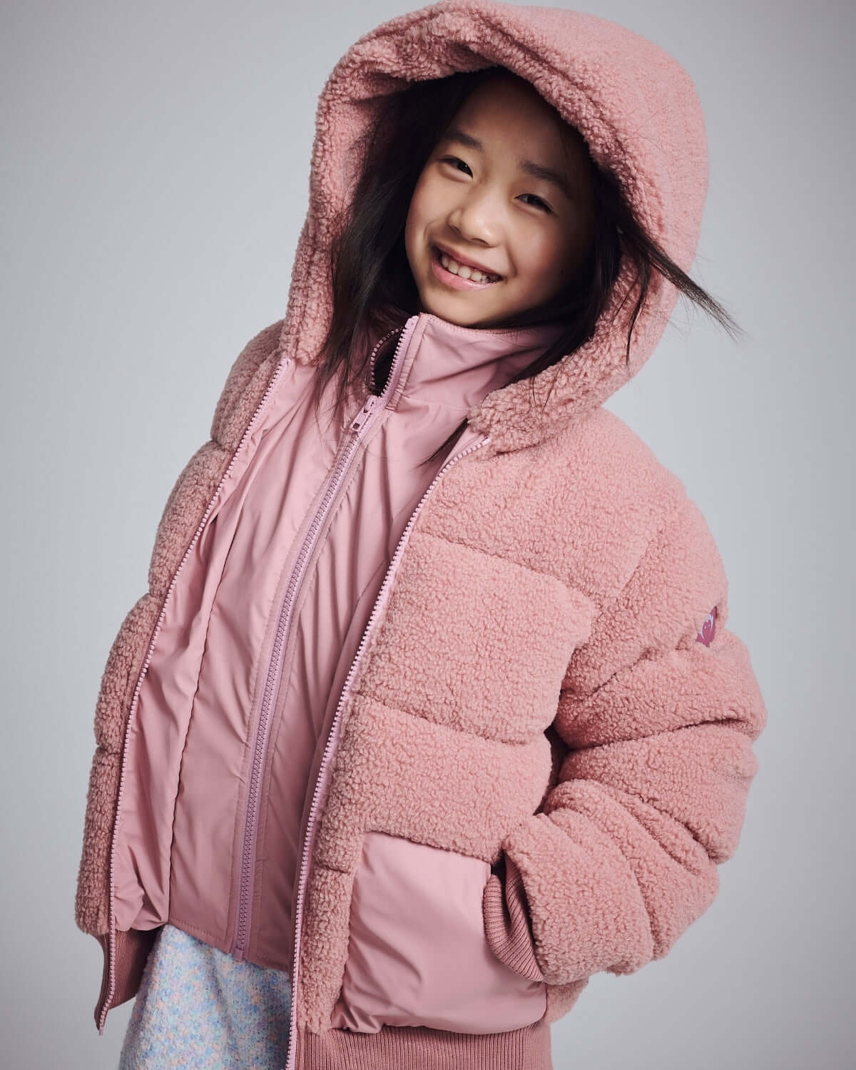 Pink Teddy Puffer Coat worn by a smiling girl, showcasing its plush sherpa material and cozy hood.