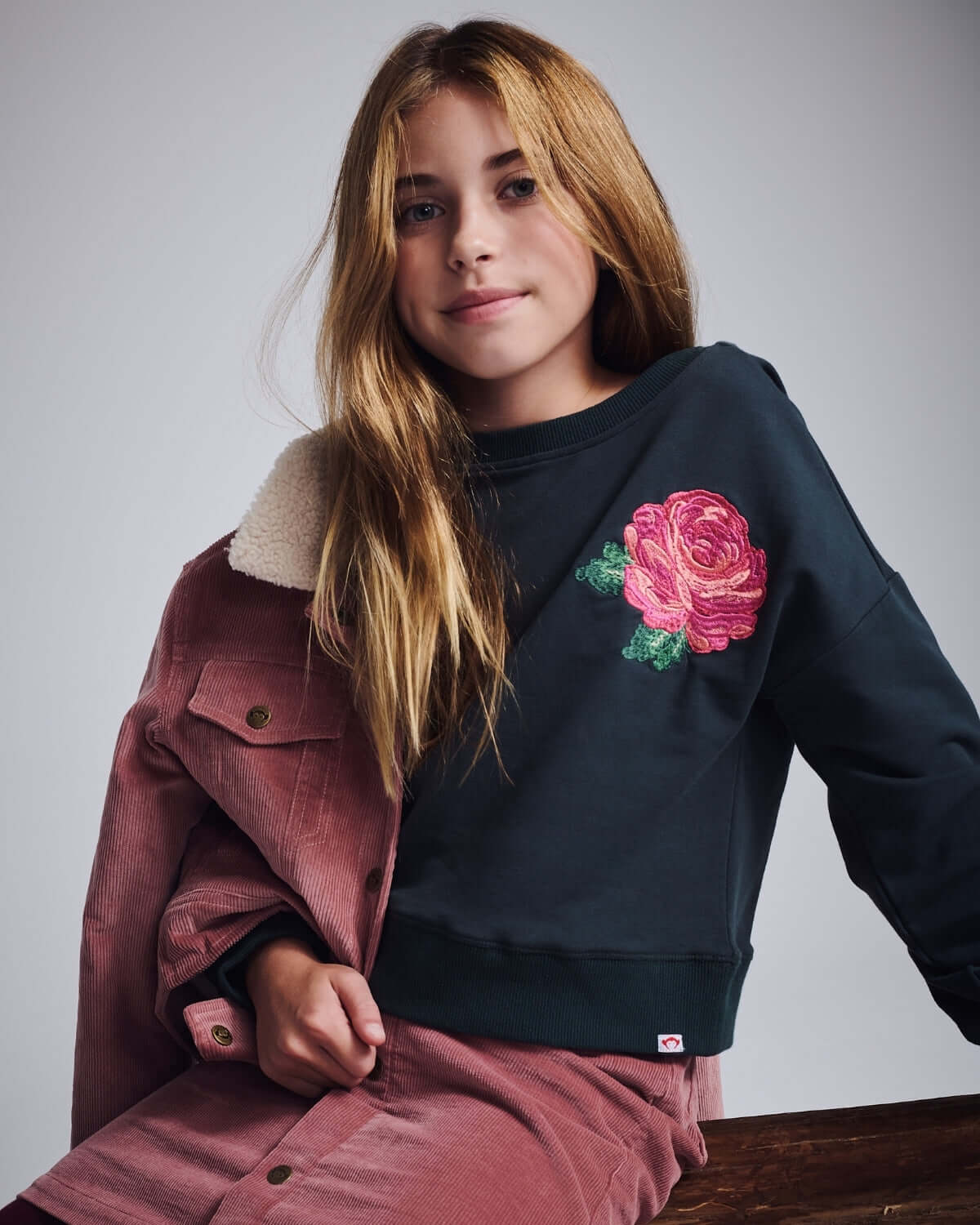 Rose Lisa Cropped Sweatshirt worn by a girl, featuring a pink rose embroidery and styled with a pink jacket.