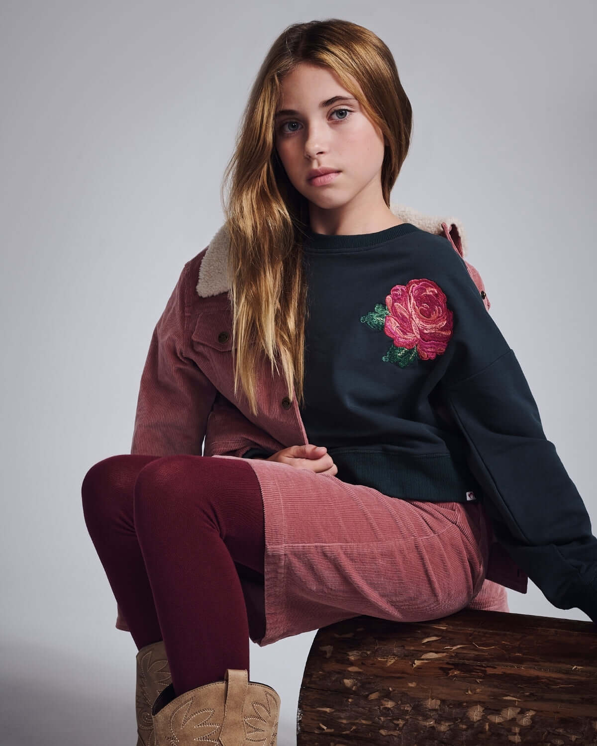 Rose Lisa Cropped Sweatshirt worn by a girl sitting on a log, showcasing its pink rose detail and cozy style.