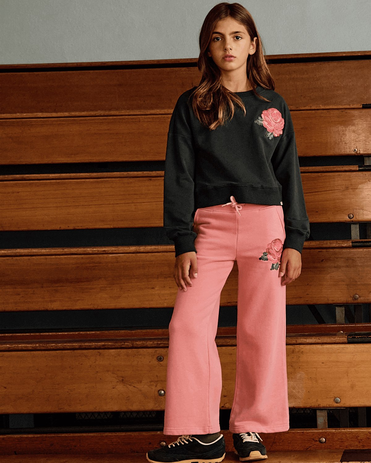 Girl wearing Rose Samantha Sweatpants with rose detail, styled with a black sweatshirt in a cozy setting.