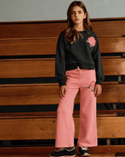 Girl wearing Rose Samantha Sweatpants with rose detail, styled with a black sweatshirt in a cozy setting.