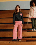 Rose Samantha Sweatpants in pink worn by a girl on bleachers, paired with a black sweatshirt and stylish sneakers.