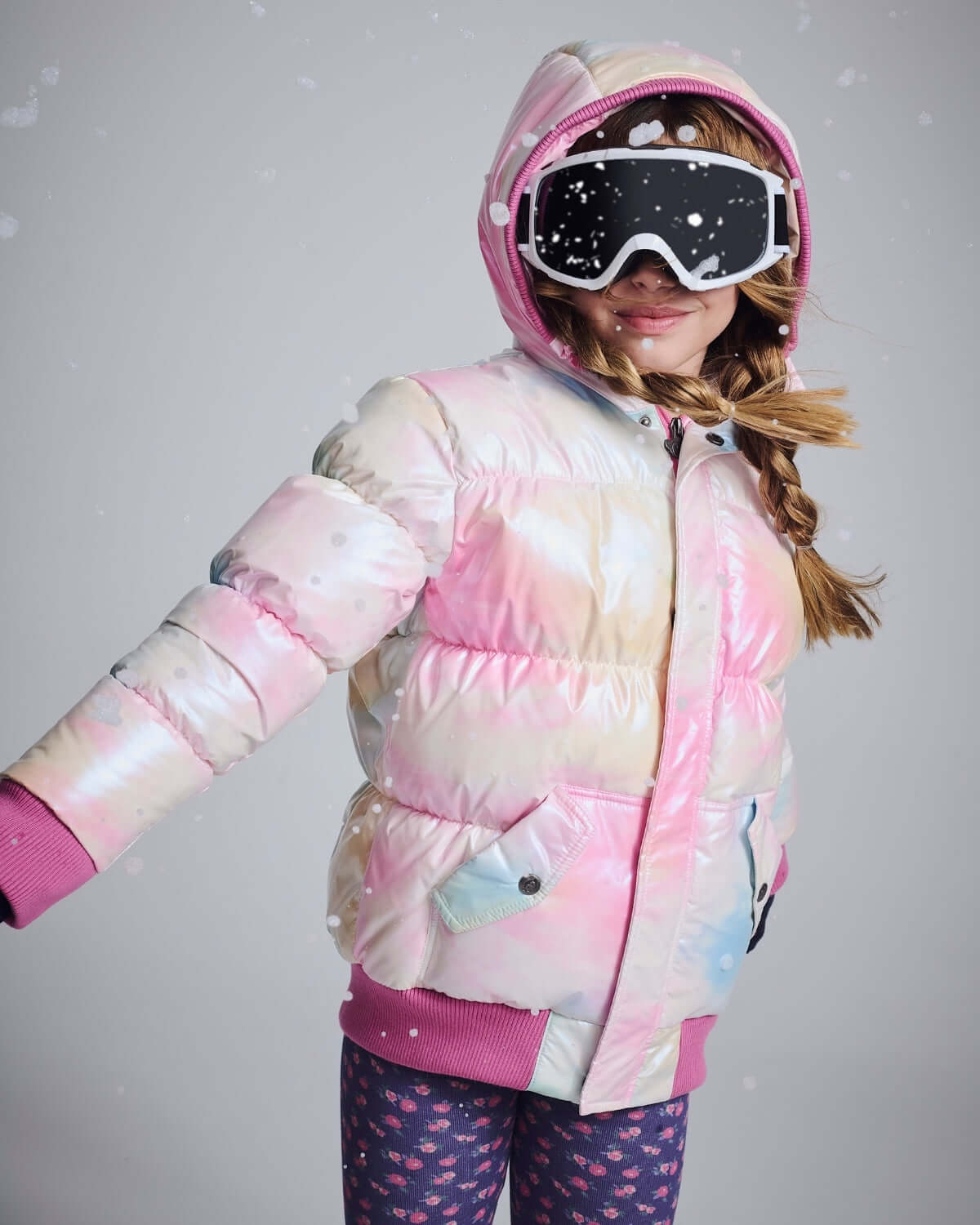 Girl wearing Iridescent Pink Slim Puffy Coat with ski goggles, showcasing the vibrant pink, blue, and cream design in snowy setting.