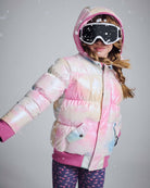 Girl wearing Iridescent Pink Slim Puffy Coat with ski goggles, showcasing the vibrant pink, blue, and cream design in snowy setting.