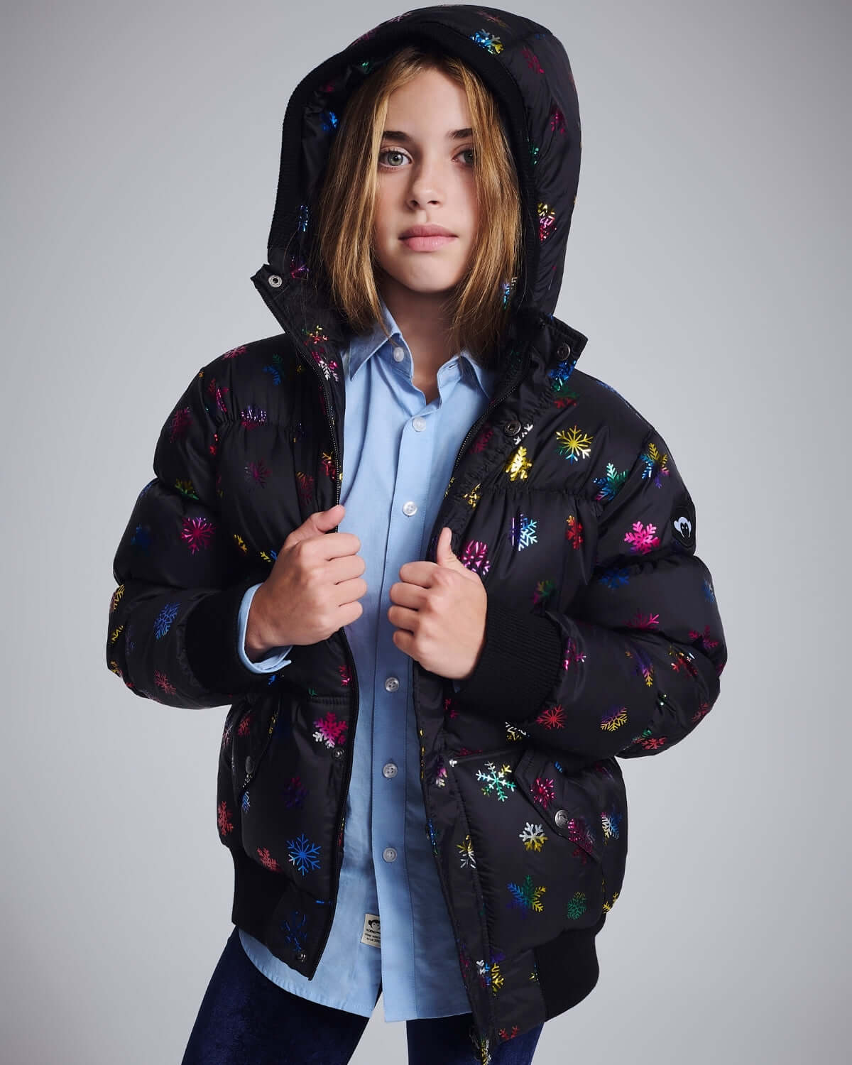 Girl wearing the Rainbow Snowflakes Slim Puffy Coat featuring a colorful snowflake design and a hood.