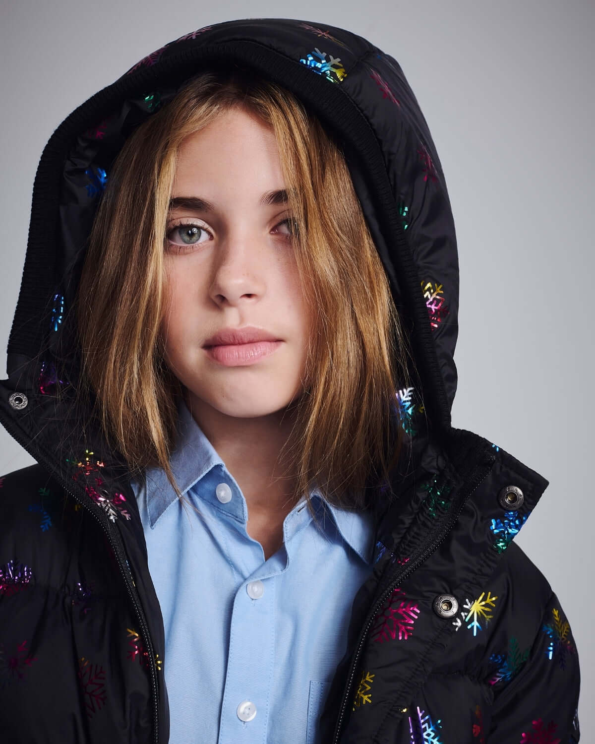 Rainbow Snowflakes Slim Puffy Coat worn by a young girl with a hood, featuring colorful snowflake designs.