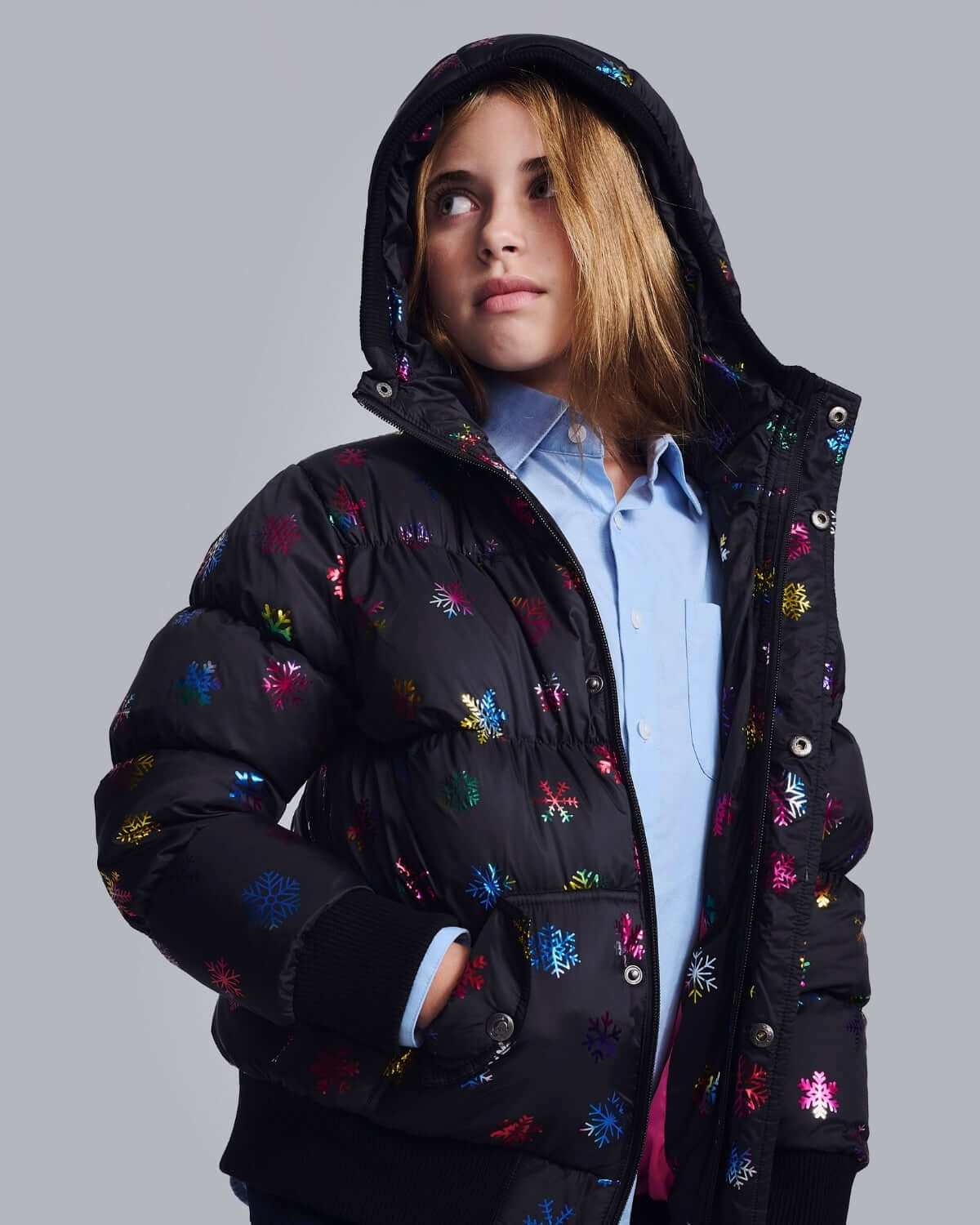 Girl wearing Rainbow Snowflakes Slim Puffy Coat with colorful snowflake designs against gray background.