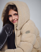 Beige Teddy Puffer Coat on a smiling girl, showcasing its cozy sherpa-lined design and plush hood.