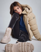 Girl wearing a Beige Teddy Puffer Coat with a plush hood and stylish boots while sitting.