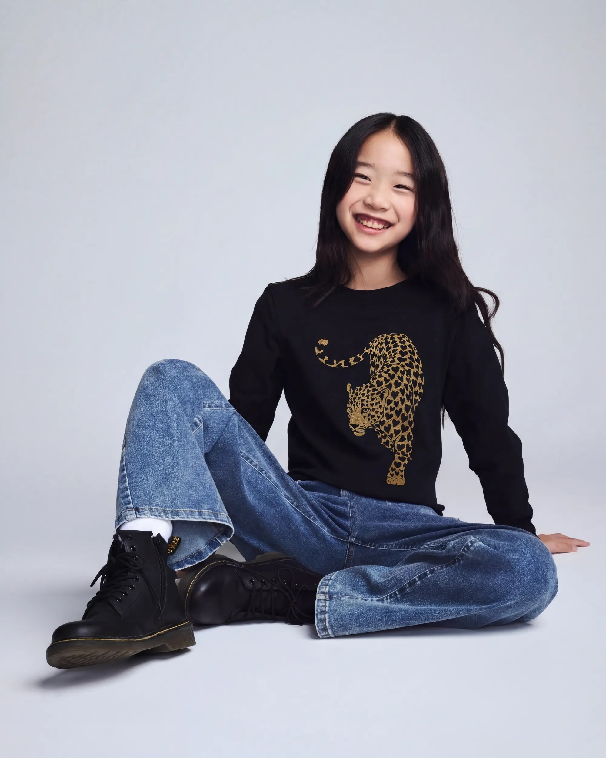 Leopard Black Elara Tee showcasing a smiling girl in black tee with leopard print design and relaxed jeans.