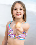 Girl smiling in Waves Stella Bikini, holding a shell at the beach, enjoying summer fun.