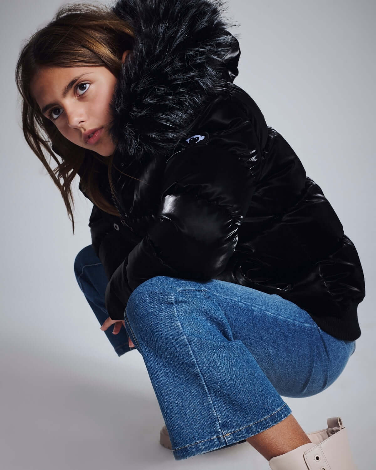 Girl in black puffer jacket and Medium Wash Wide Leg Jeans, crouching pose for stylish winter look.
